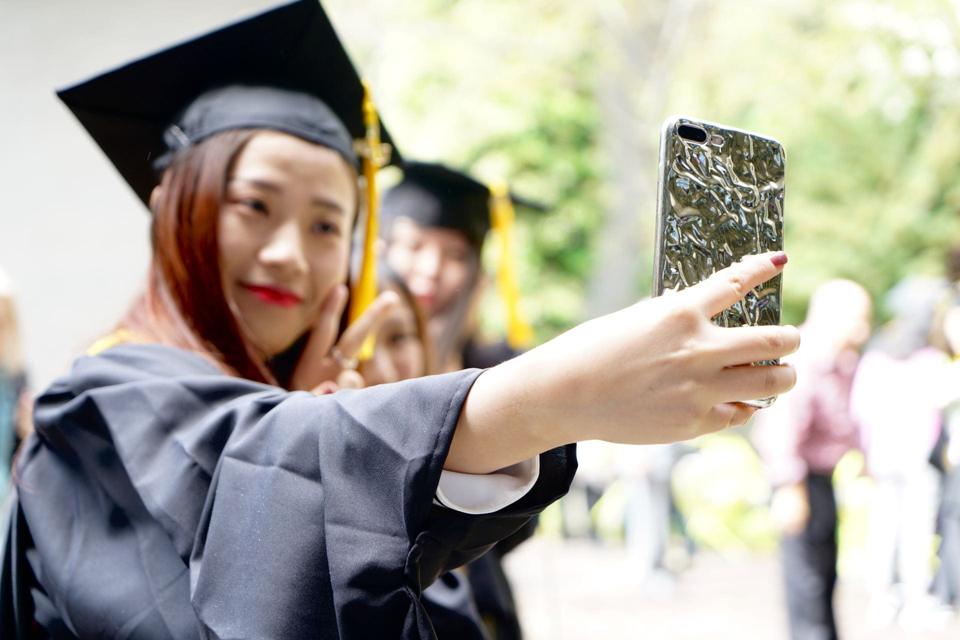 Woman in regalia holding phone taking a selfie
